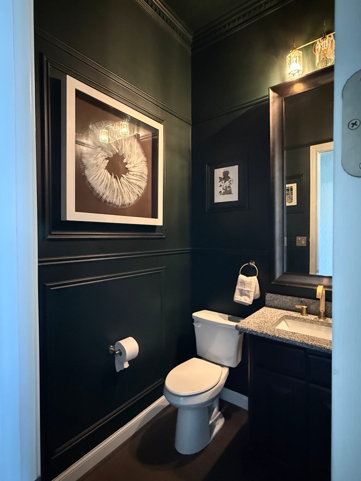 Powder room after remodel: deep green walls, custom picture-frame molding, brushed-brass fixtures and crystal sconces