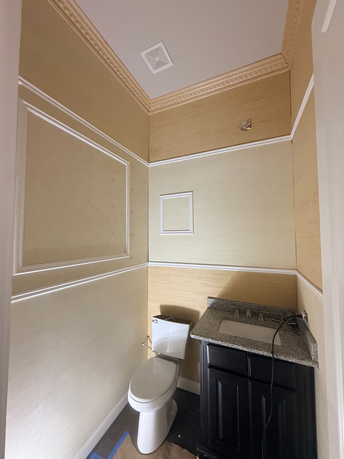 The same powder room before the remodel: dated tan grasscloth wallpaper and basic fixtures